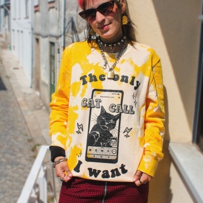 Pessoa com camisola amarela e creme com gato e texto, saia vermelha xadrez, meias de rede e acessórios