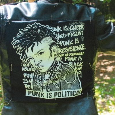 Casaco de pele preto com aplicação têxtil punk preta e branca nas costas com ilustração e texto