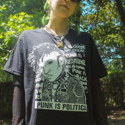Pessoa com t-shirt preta estampada com rosto e texto PUNK IS POLITICAL ao ar livre