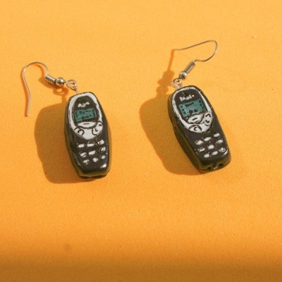 Brincos em forma de telemóveis antigos sobre fundo laranja.