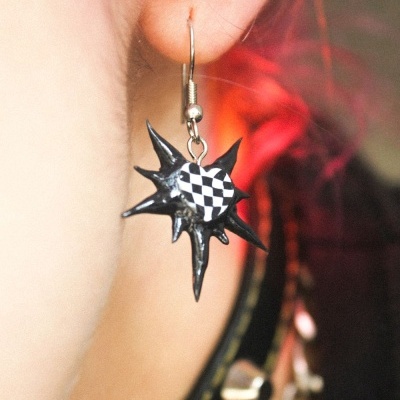 Brinco pendente preto com padrão xadrez preto e branco no centro.