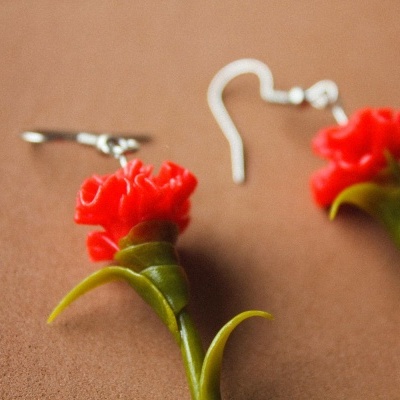 brincos com flores vermelhas e folhas verdes sobre fundo castanho