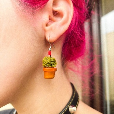 Brinco em forma de vaso de planta pendurado na orelha de pessoa com cabelo cor-de-rosa.