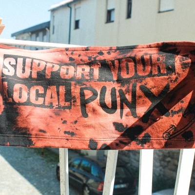 Máscara facial em tecido laranja e preto com texto e ilustrações pendurada em corrimão branco