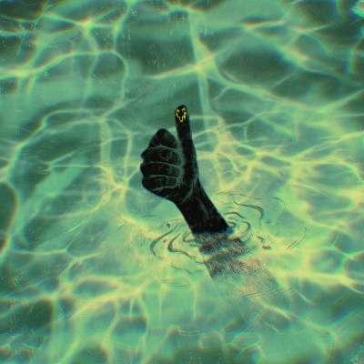 Mão negra submersa com polegar para cima e carinha amarela sorridente no dedo em líquido verde-azulado