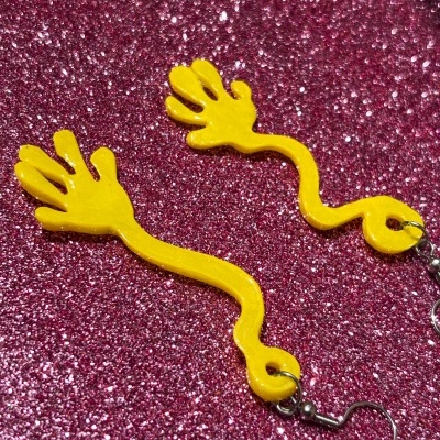 Brincos amarelos em forma de mãos sobre fundo rosa brilhante