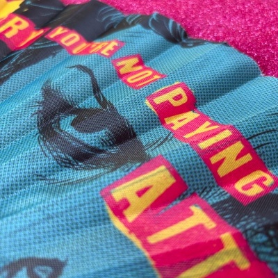 Máscara azul com estampa e texto em rosa e amarelo ao lado de pano rosa com bolinhas