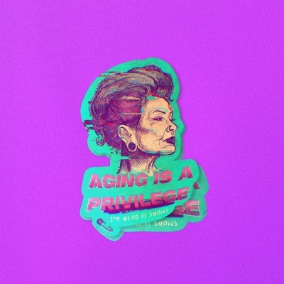 Adesivo de mulher idosa com texto AGING IS A PRIVILEGE e IM GLAD IT SHOWS em fundo roxo