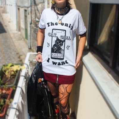 Pessoa com t-shirt branca estampada, saia xadrez e botas pretas com atacadores amarelos