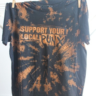 T-shirt tie-dye preta e castanha com texto em laranja pendurada num varal