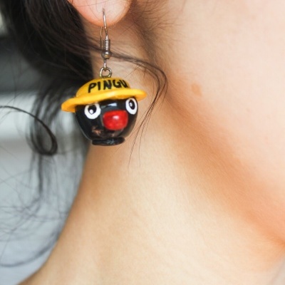Brinco pendente de figura negra com chapéu amarelo e inscrição PINGU