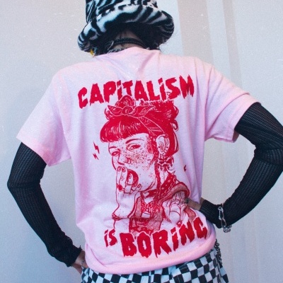 Pessoa de costas veste t-shirt rosa com estampa vermelha, calças de xadrez preto e branco e chapéu estampado preto e branco.