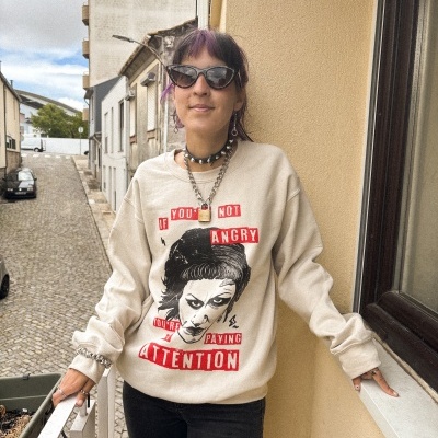 Mulher de óculos escuros com camisola bege estampada com texto em fundo urbano