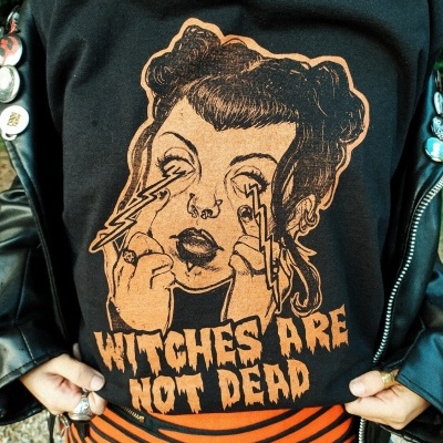 Camisola preta com estampa laranja e texto WITCHES ARE NOT DEAD