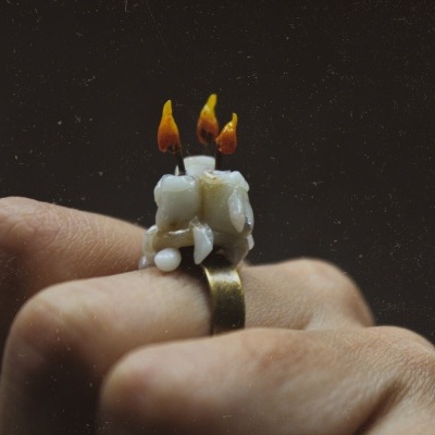 Anel dourado com velas brancas acesas num dedo