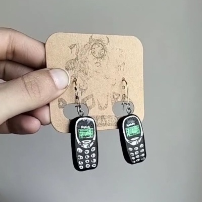 Brincos com design de telemóveis antigos pretos e verdes em cartão castanho com desenho de cão.