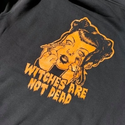 Sweatshirt preta com estampa laranja e texto WITCHES ARE NOT DEAD.