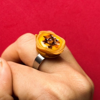 Anel prateado com pedra amarela, mão com fundo vermelho