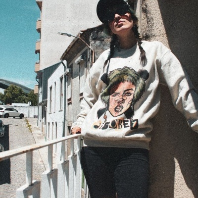 Pessoa com sweatshirt branca estampada com rosto estilizado e texto OBEY, collants de rede com buracos, óculos escuros e boné preto.