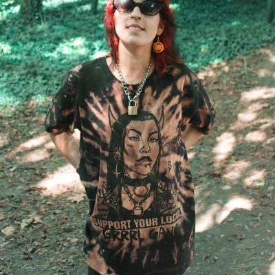 Pessoa de cabelo vermelho a usar t-shirt tie-dye com ilustração e texto em floresta