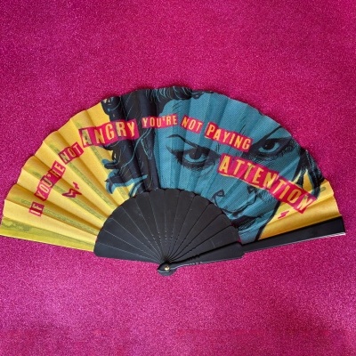 Leque colorido com rosto desenhado e texto em fundo rosa brilhante.