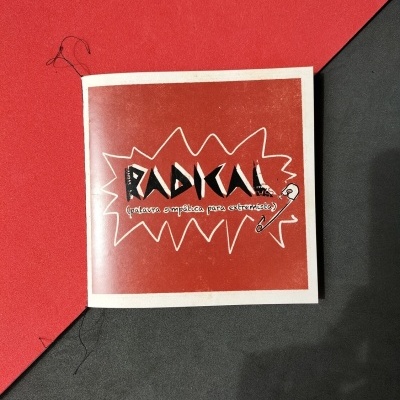 Livro ou caderno vermelho e branco com texto RADICAL e alfinete de segurança