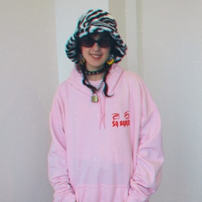 Pessoa com sweatshirt rosa claro com estampa vermelha, chapéu zebra e acessórios