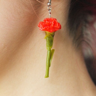 Brinco pendente com flor vermelha e caule verde na orelha