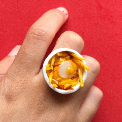 Anel branco com pintura de comida em dedo sobre fundo vermelho