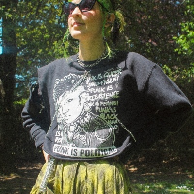 Mulher com sweatshirt preta com texto e saia plissada amarela em ambiente exterior