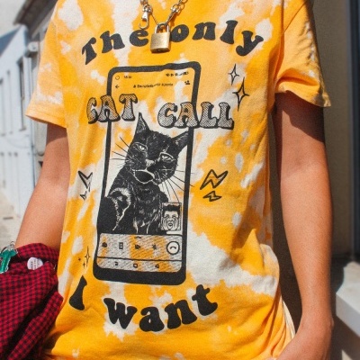 T-shirt amarela tie-dye com ilustração de gato e texto em preto