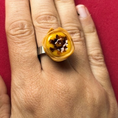 Anel com topo que parece uma pequena tartelette amarela com detalhes castanhos