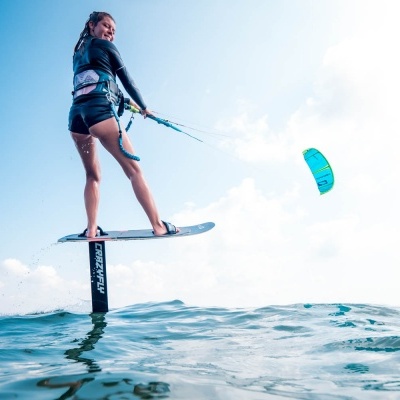 Mulher a praticar kite foil surf em mar com prancha e pipa azul e verde