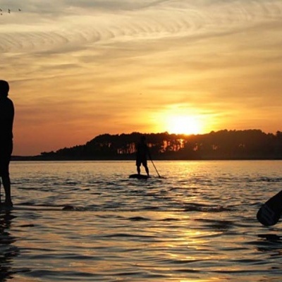 Três pessoas a praticar paddleboard ao pôr do sol na água