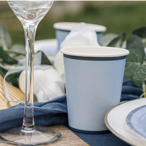 Copo de papel azul claro com borda azul escura em mesa posta ao ar livre