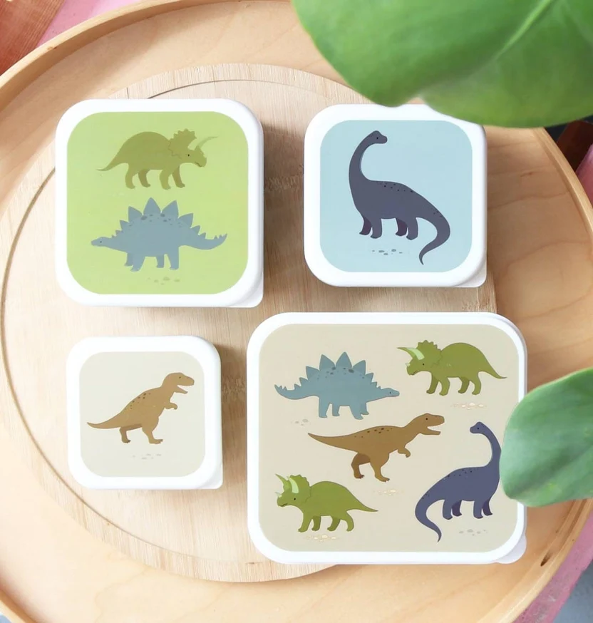 Set 4 Lancheiras : Dinossauros Caixas de plástico com ilustrações de dinossauros coloridos em diferentes tamanhos sobre um tabuleiro de madeira.