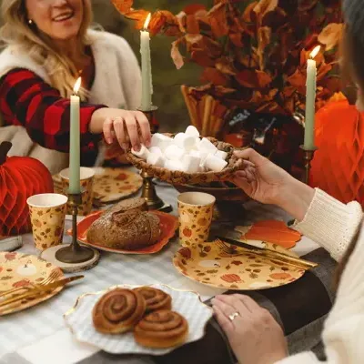 Mesa decorada com tema outonal para lanche com bolos, pão, marshmallows e decoração de abóboras e velas acesas