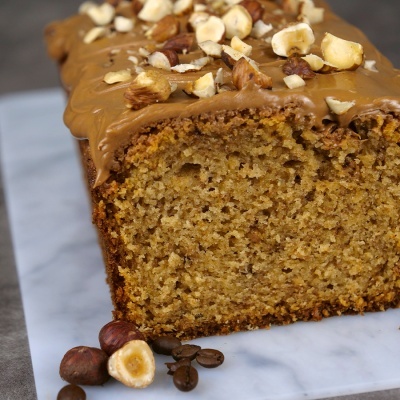 Bolo com cobertura castanha e avelãs sobre base branca com grãos de café e avelãs ao lado