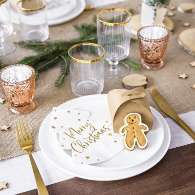 Mesa posta com decoração natalícia, pratos, guardanapos, biscoito gingerbread e copos com rebordo dourado.