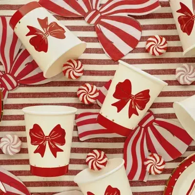 Copos de papel com laços vermelhos sobre toalha listrada vermelha e branca com doces