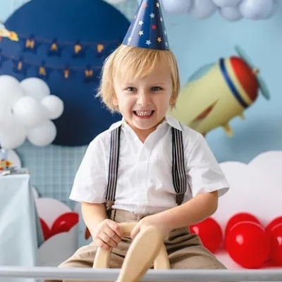 Criança com chapéu de festa e avião de madeira em ambiente com balões coloridos