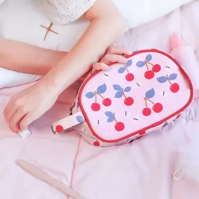 Necessaire rosa com padrão de cerejas ao lado de braços e produtos de higiene