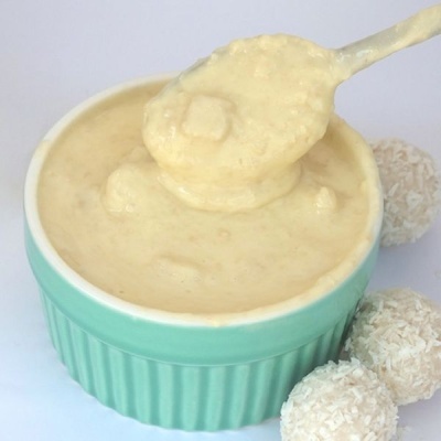 Creme creme numa taça verde com colher e bolas de coco ao lado