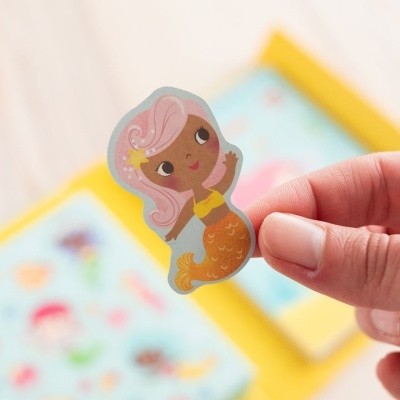 Adesivo infantil de sereia com cabelo rosa e cauda laranja na mão