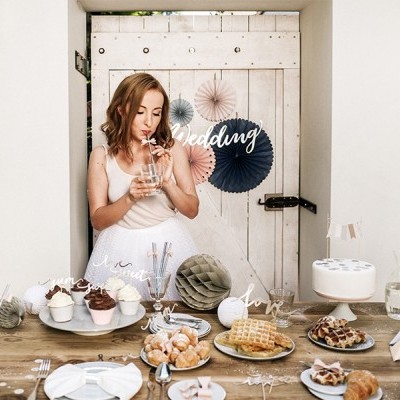 Mulher em vestido branco ao lado de mesa com doces e decoração de casamento
