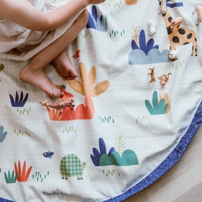 Tapete redondo infantil colorido com padrão de animais e plantas, borda azul e brinquedos em cima
