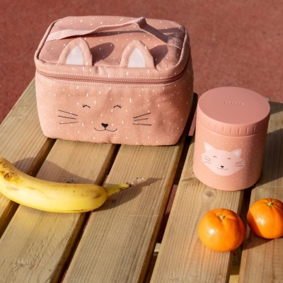 Estojo rosa com rosto de gato e recipiente rosa com tampa, banana e tangerinas sobre banco de madeira.