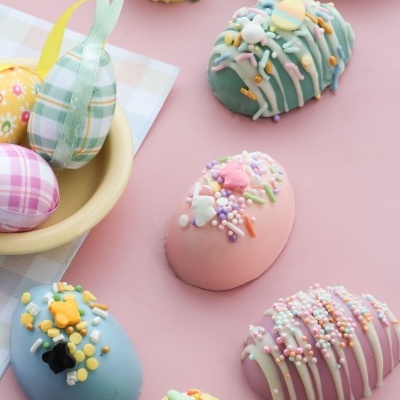 Ovos de chocolate decorados em cores pastel com confeitos coloridos sobre superfície rosa