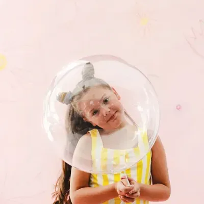 Menina com blusa amarela e riscas brancas dentro de bolha de sabão transparente