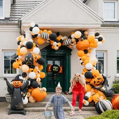 Arco de balões de Halloween em tons laranja, preto e branco com abóboras à frente de casa